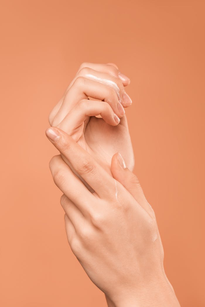 creative-03 Close-up of hands with oil on peach background, emphasizing skincare and wellness.